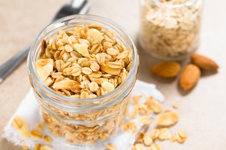 Coconut Almond granola in glass jar, ingredients and spoon in the background.